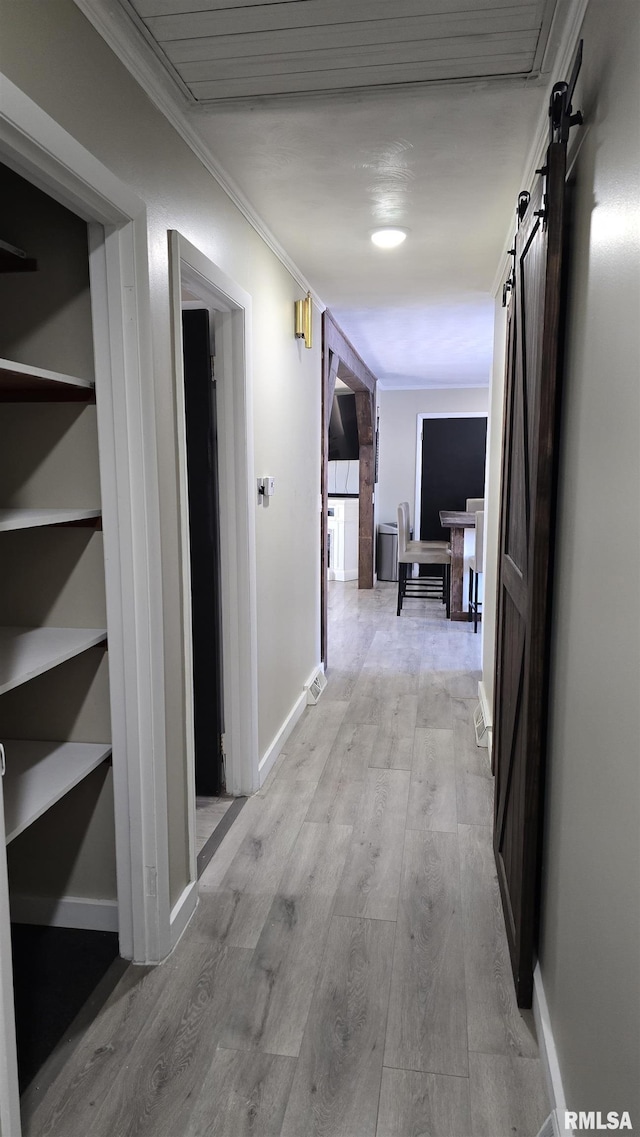 corridor featuring a barn door, ornamental molding, and light hardwood / wood-style floors