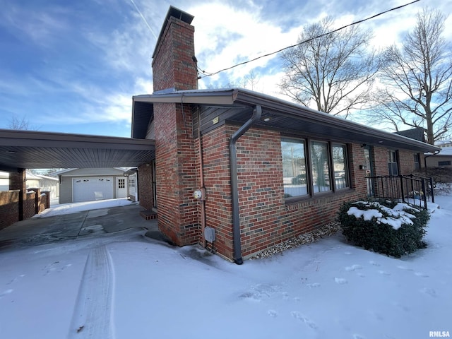 view of snowy exterior featuring a garage, an outdoor structure, and a carport