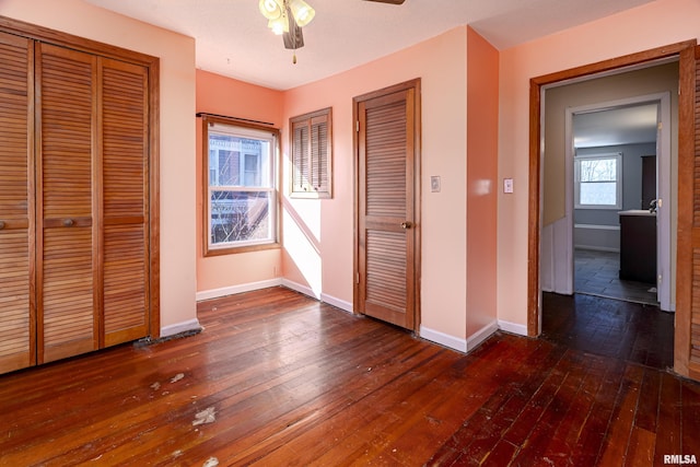 unfurnished bedroom with ceiling fan, dark hardwood / wood-style floors, and two closets