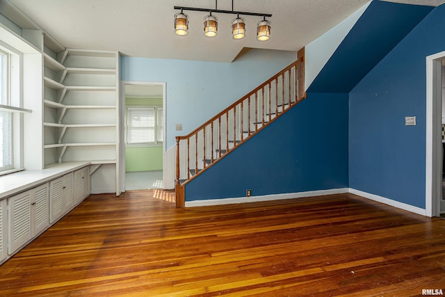 unfurnished living room with hardwood / wood-style floors, built in features, a textured ceiling, and a healthy amount of sunlight