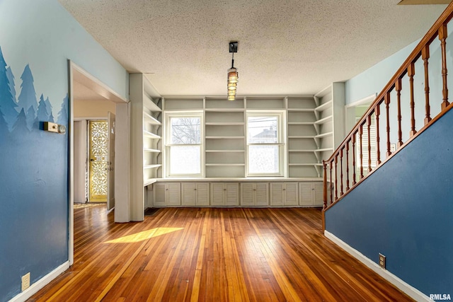 unfurnished dining area with a textured ceiling, wood-type flooring, and built in shelves