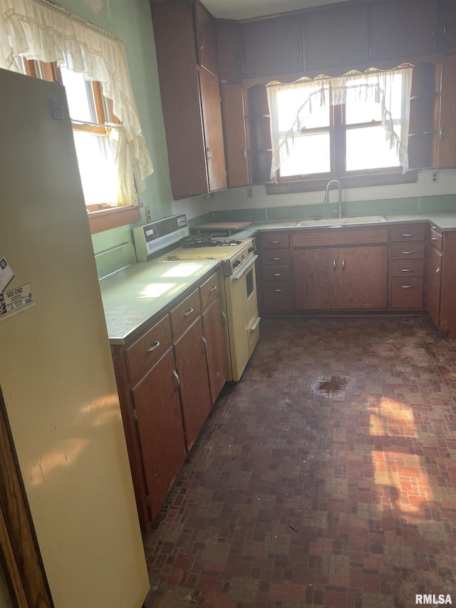 kitchen with white gas stove, freestanding refrigerator, a sink, light countertops, and brick patterned floor