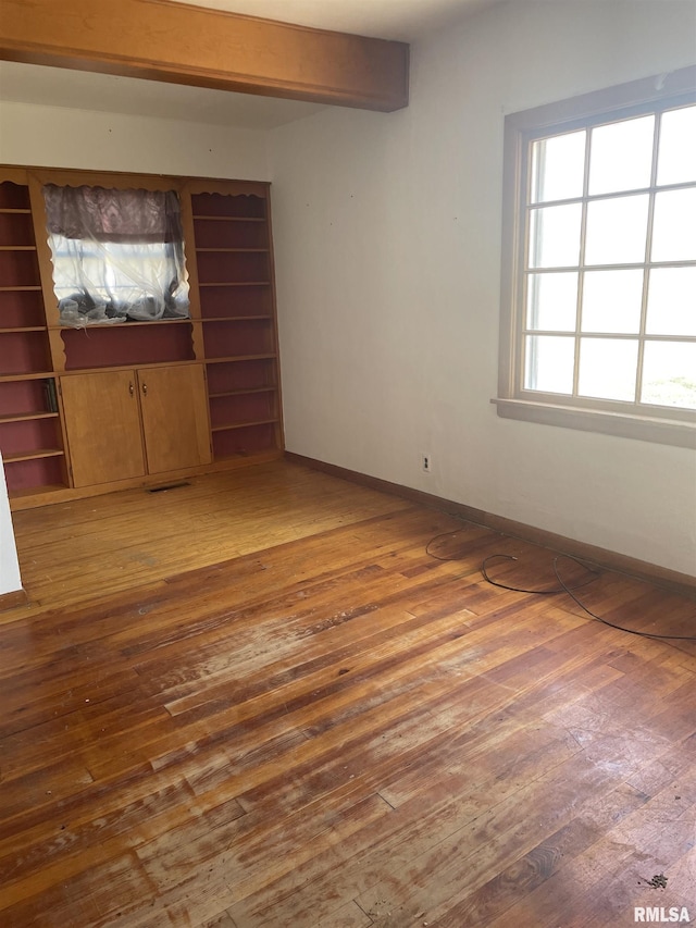 unfurnished bedroom with hardwood / wood-style floors, beam ceiling, visible vents, and baseboards