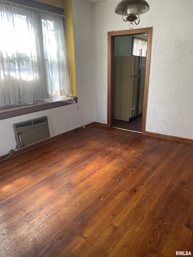 empty room featuring an AC wall unit, a textured wall, baseboards, and wood-type flooring