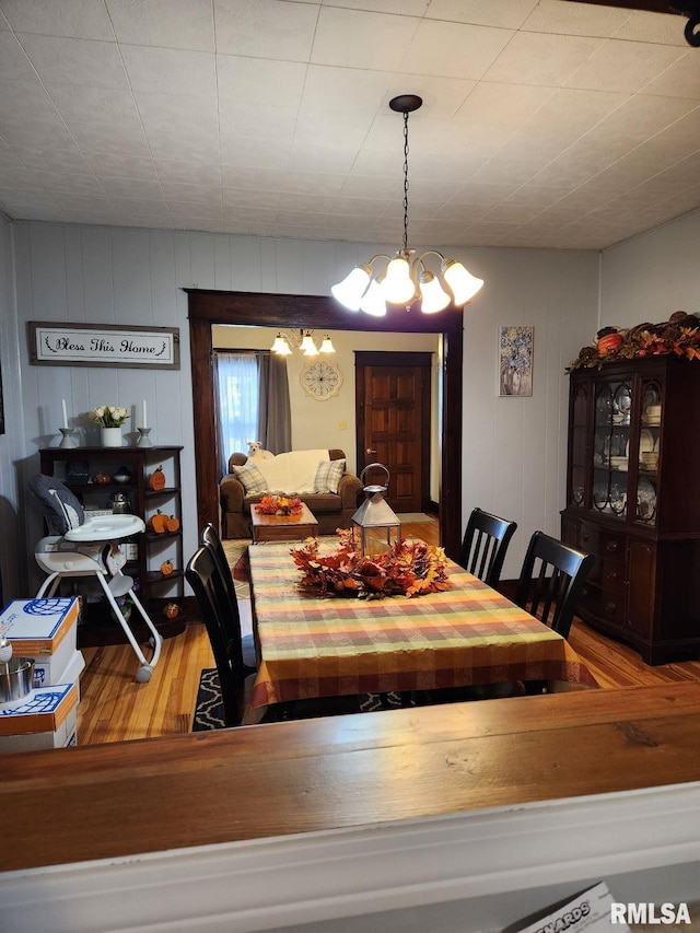 dining area with hardwood / wood-style floors, a chandelier, and wooden walls