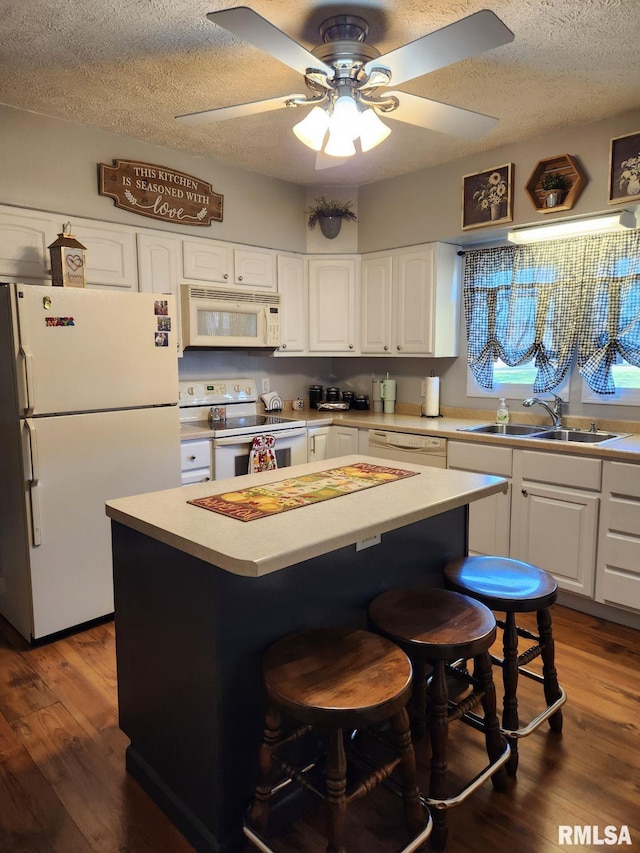 kitchen with white appliances, a textured ceiling, a kitchen island, white cabinets, and sink