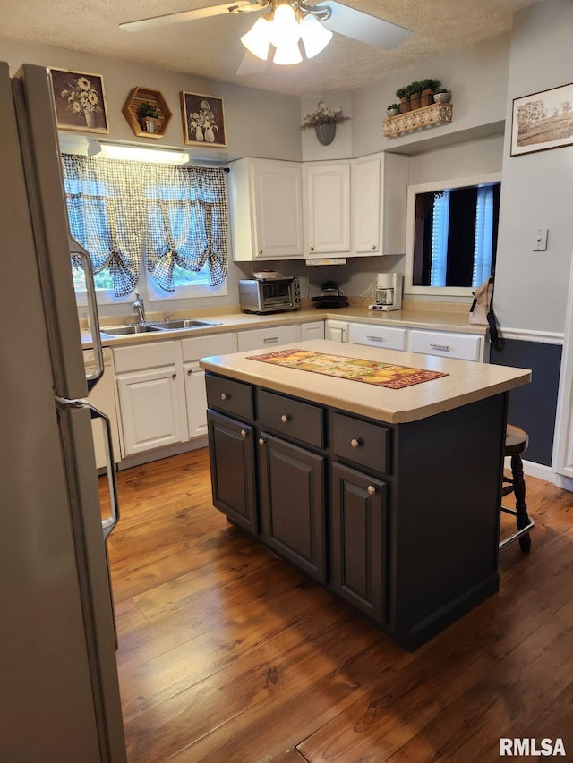 kitchen featuring dark hardwood / wood-style floors, a kitchen island, sink, stainless steel refrigerator, and white cabinets