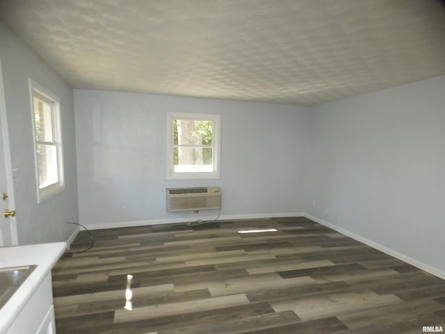 unfurnished room with an AC wall unit, dark hardwood / wood-style floors, sink, and a textured ceiling