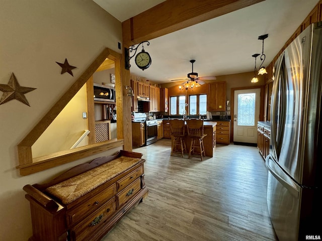 kitchen with appliances with stainless steel finishes, a center island, hanging light fixtures, light wood-type flooring, and a breakfast bar