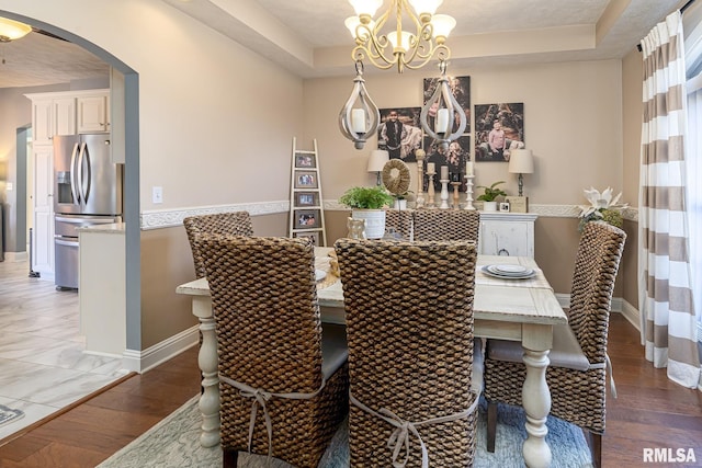 dining space with dark wood-type flooring, a notable chandelier, and a tray ceiling