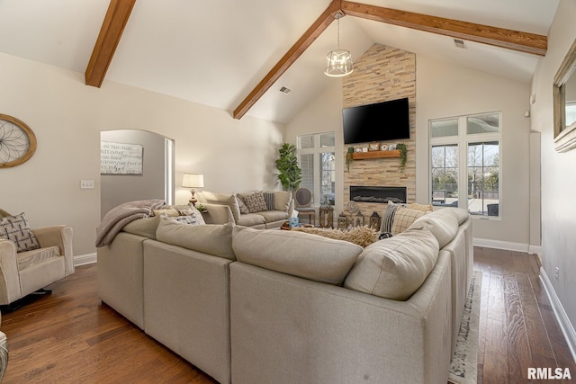 living area with arched walkways, a stone fireplace, baseboards, and beamed ceiling