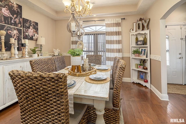 dining space with arched walkways, a chandelier, dark wood-style flooring, a raised ceiling, and baseboards