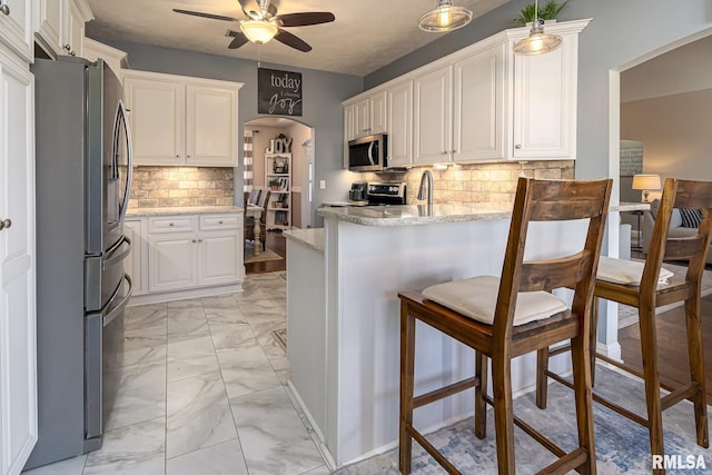kitchen with ceiling fan, light stone countertops, a peninsula, marble finish floor, and stainless steel appliances