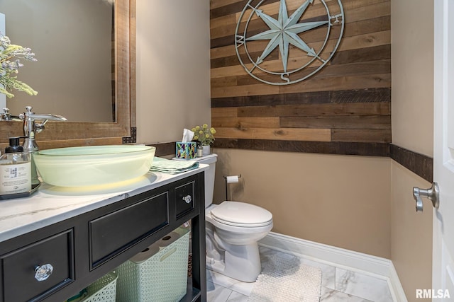 bathroom featuring toilet, wood walls, and vanity