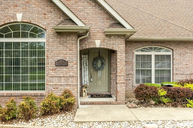 entrance to property featuring brick siding and a shingled roof