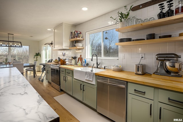 kitchen with appliances with stainless steel finishes, green cabinetry, decorative backsplash, sink, and light hardwood / wood-style flooring