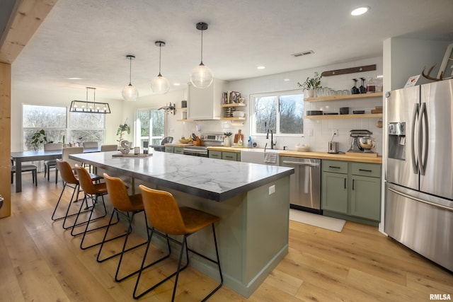 kitchen with green cabinetry, a kitchen island, light hardwood / wood-style flooring, backsplash, and stainless steel appliances