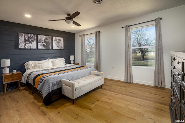 bedroom featuring ceiling fan, wood walls, light hardwood / wood-style floors, and a textured ceiling