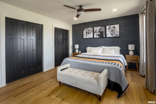 bedroom with ceiling fan, light wood-type flooring, multiple closets, and wooden walls