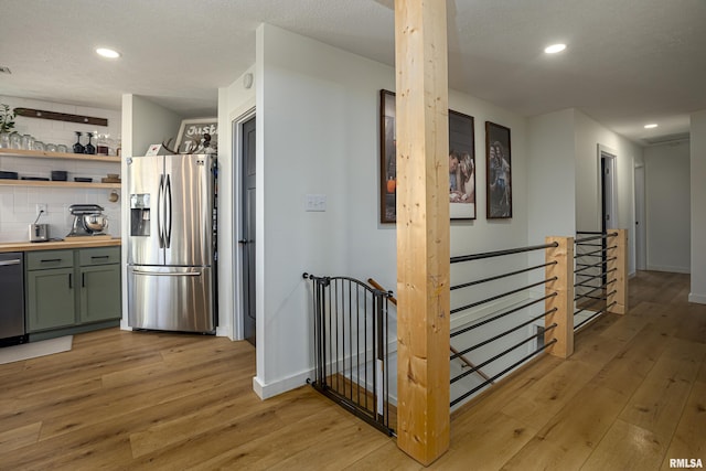 kitchen with a textured ceiling, appliances with stainless steel finishes, tasteful backsplash, green cabinets, and light hardwood / wood-style flooring