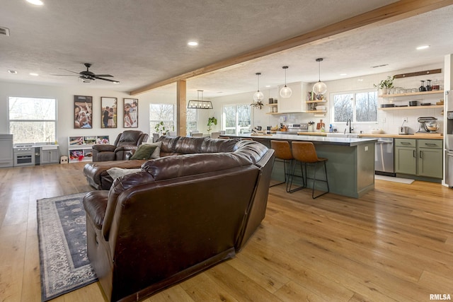 living room featuring sink, beam ceiling, light hardwood / wood-style floors, and a textured ceiling