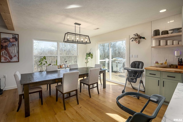 dining space featuring an inviting chandelier, a textured ceiling, beam ceiling, and light wood-type flooring