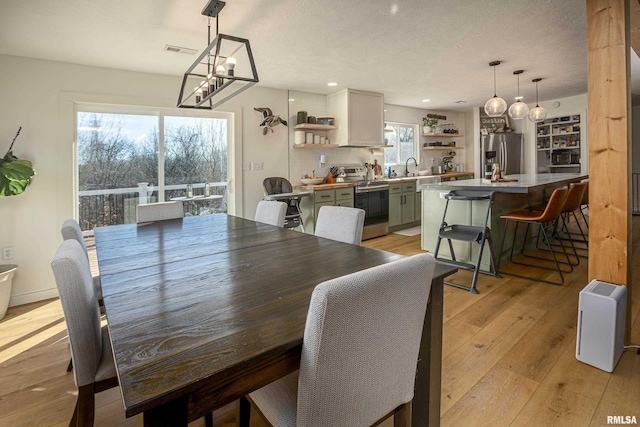 dining area featuring sink, a textured ceiling, a chandelier, and light wood-type flooring