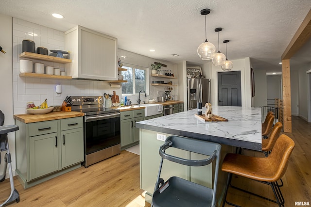 kitchen featuring a textured ceiling, stainless steel appliances, backsplash, green cabinetry, and light wood-type flooring