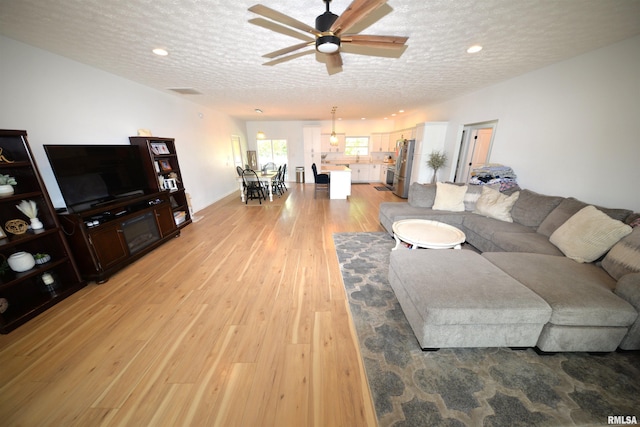 living room with light hardwood / wood-style floors, a textured ceiling, and ceiling fan