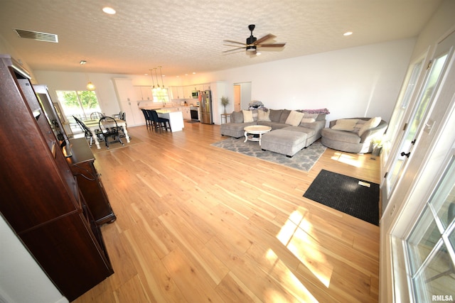 living room with ceiling fan, a textured ceiling, and light hardwood / wood-style flooring