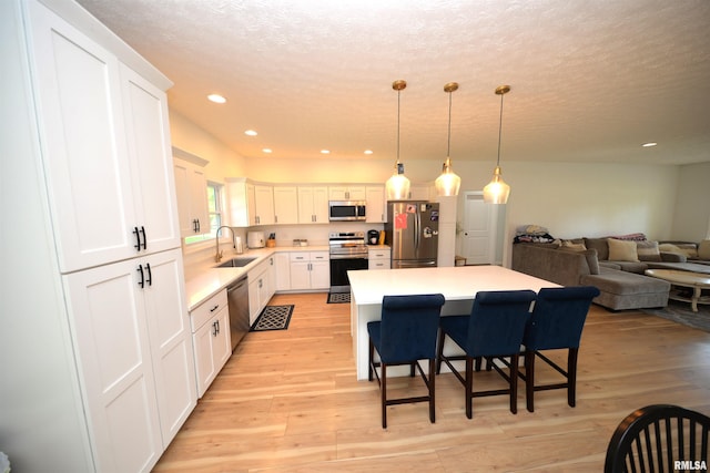 kitchen featuring pendant lighting, sink, white cabinets, a kitchen bar, and stainless steel appliances