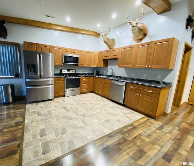 kitchen featuring appliances with stainless steel finishes, sink, a high ceiling, beam ceiling, and dark stone counters