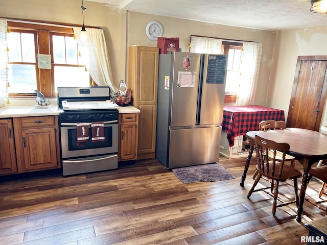 kitchen with decorative light fixtures, a textured ceiling, appliances with stainless steel finishes, and dark hardwood / wood-style flooring