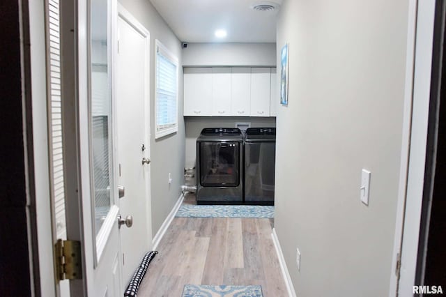 clothes washing area with washing machine and clothes dryer, light hardwood / wood-style floors, and cabinets