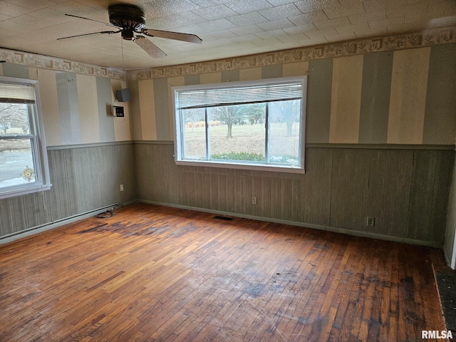 unfurnished room featuring wood walls, a baseboard radiator, dark wood-type flooring, and ceiling fan