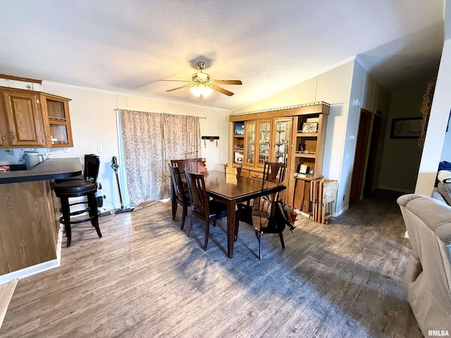 dining space featuring dark wood-type flooring, lofted ceiling, crown molding, a textured ceiling, and ceiling fan