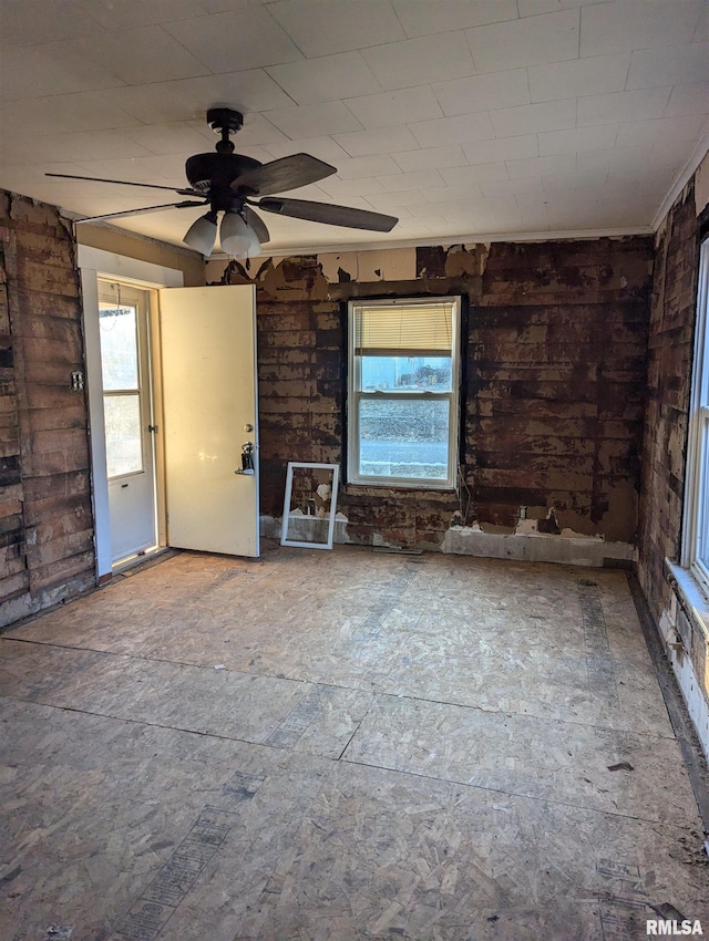 unfurnished living room with ceiling fan, plenty of natural light, and brick wall