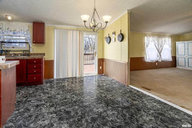 kitchen with hanging light fixtures, wooden walls, dark carpet, and a textured ceiling