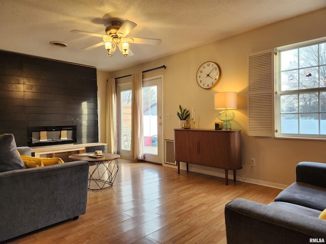 living room with ceiling fan, a fireplace, a textured ceiling, and light wood-type flooring