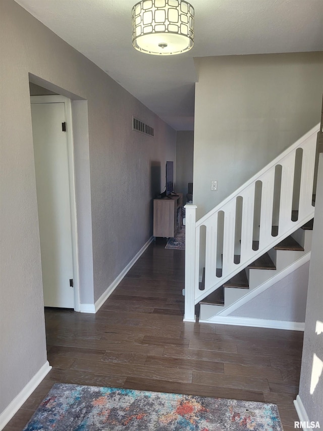 stairway featuring visible vents, baseboards, a textured wall, and wood finished floors
