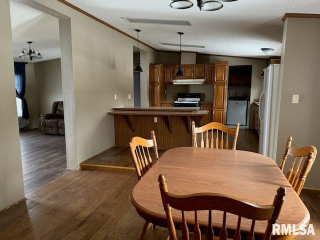 dining area featuring crown molding, a chandelier, vaulted ceiling, a textured ceiling, and dark hardwood / wood-style flooring