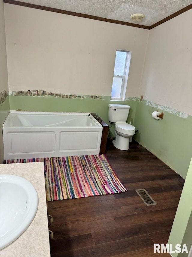 bathroom featuring a tub, hardwood / wood-style flooring, vanity, toilet, and a textured ceiling