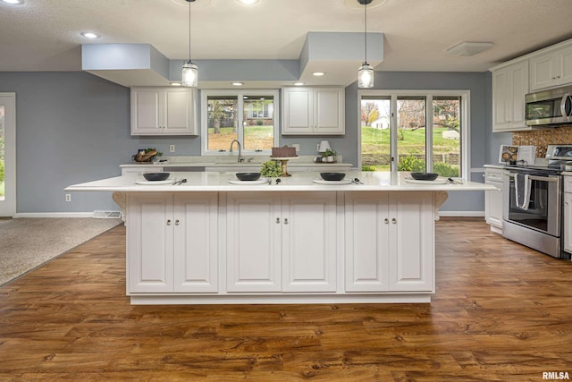 kitchen featuring stainless steel appliances, white cabinetry, a center island, and decorative light fixtures