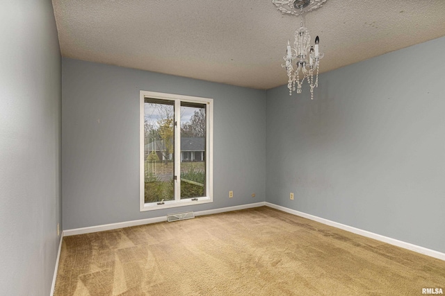 spare room with a chandelier, a textured ceiling, and carpet flooring