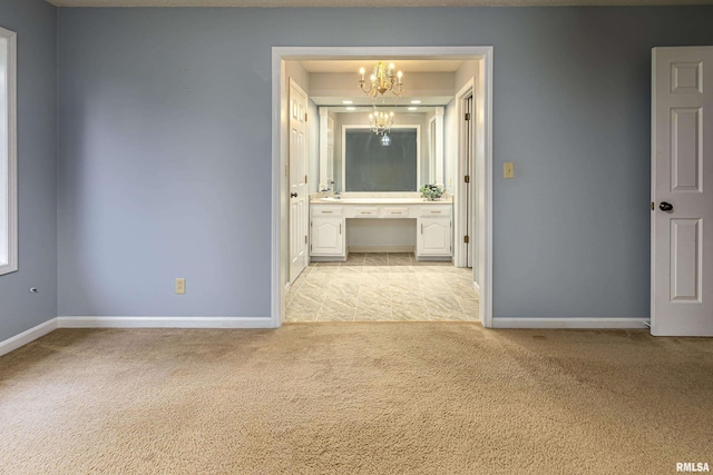 empty room with built in desk, light colored carpet, and a notable chandelier