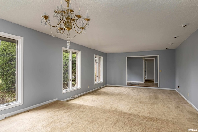 carpeted spare room with a notable chandelier and a textured ceiling