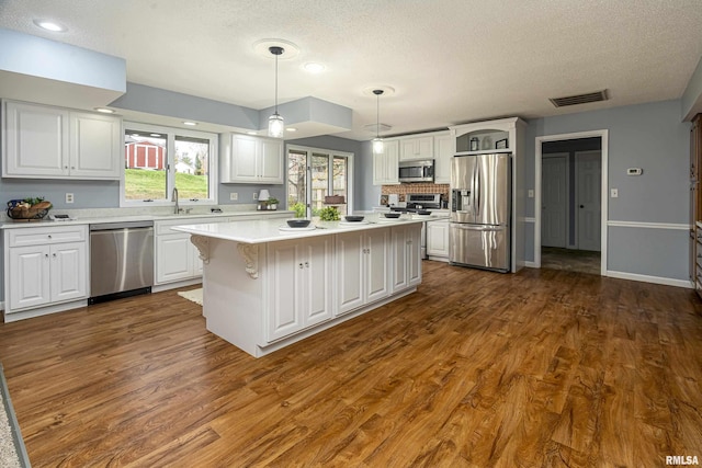 kitchen with stainless steel appliances, dark hardwood / wood-style floors, white cabinets, a kitchen island, and decorative light fixtures