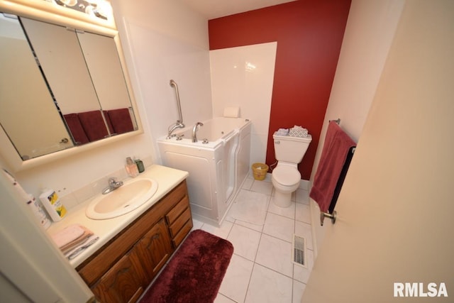 bathroom with a bathtub, tile patterned flooring, vanity, washing machine and clothes dryer, and toilet