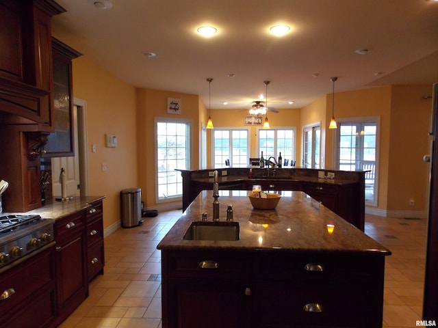 kitchen featuring light tile patterned floors, sink, stone counters, hanging light fixtures, and a large island with sink