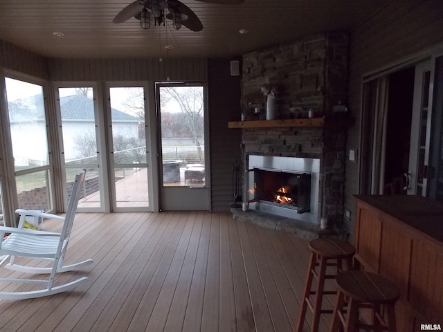 interior space with a water view, ceiling fan, a stone fireplace, and wood ceiling